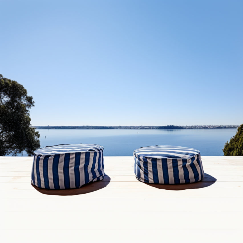 Blue and white striped ottoman bean bags sitting on a light coloured grey wooden deck overlooking the ocean 